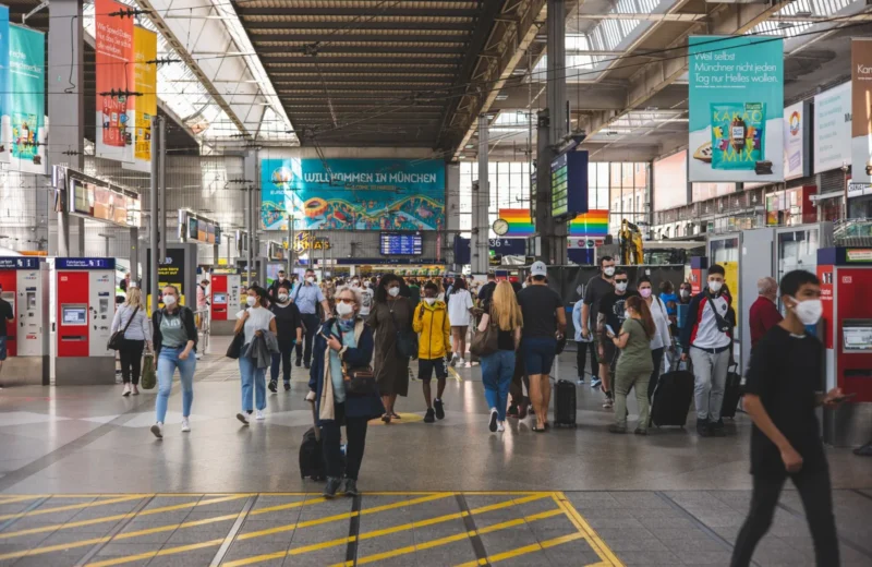 Busy scene at Munich Hauptbahnhof with masked travelers and luggage.