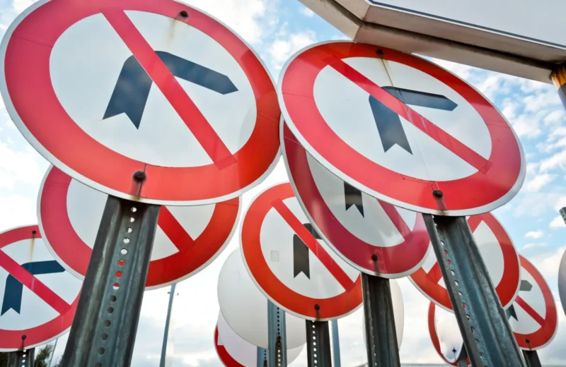 Multiple no left turn traffic signs displayed together under a blue sky.