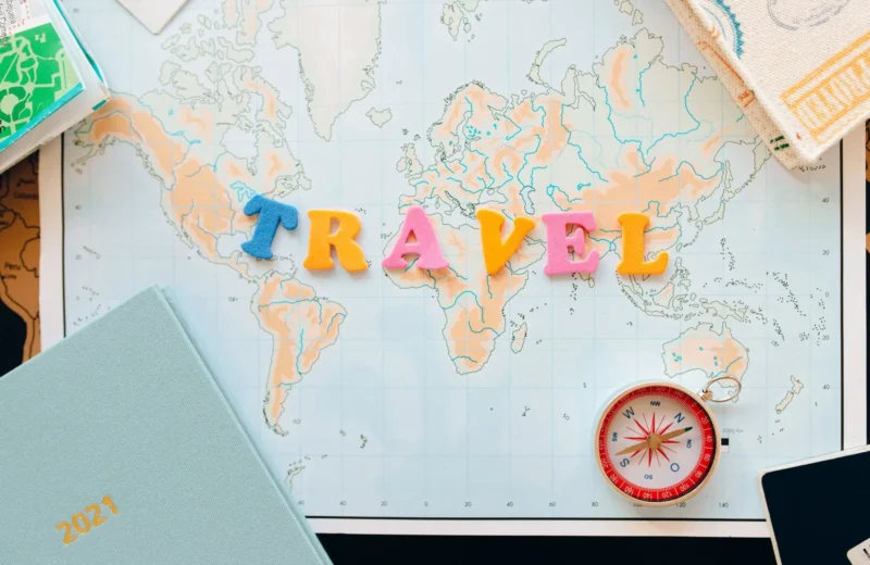 Flat lay of a map with colorful letters "TRAVEL" and a compass for planning adventures.