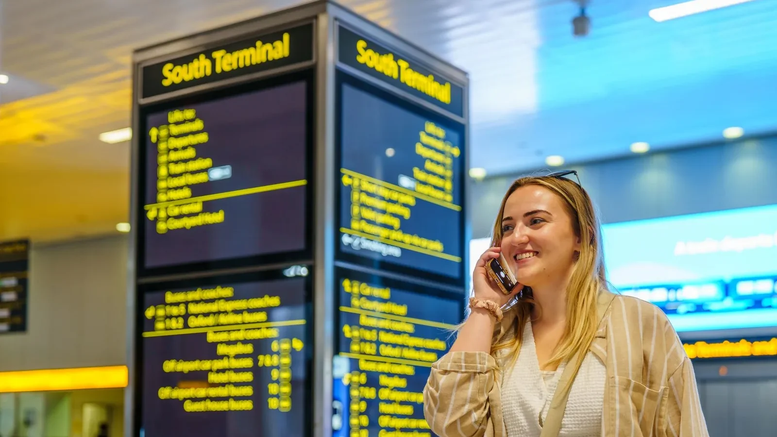 Smiling woman on phone in South Terminal of Gatwick Airport, Horley, enjoying her travel experience.