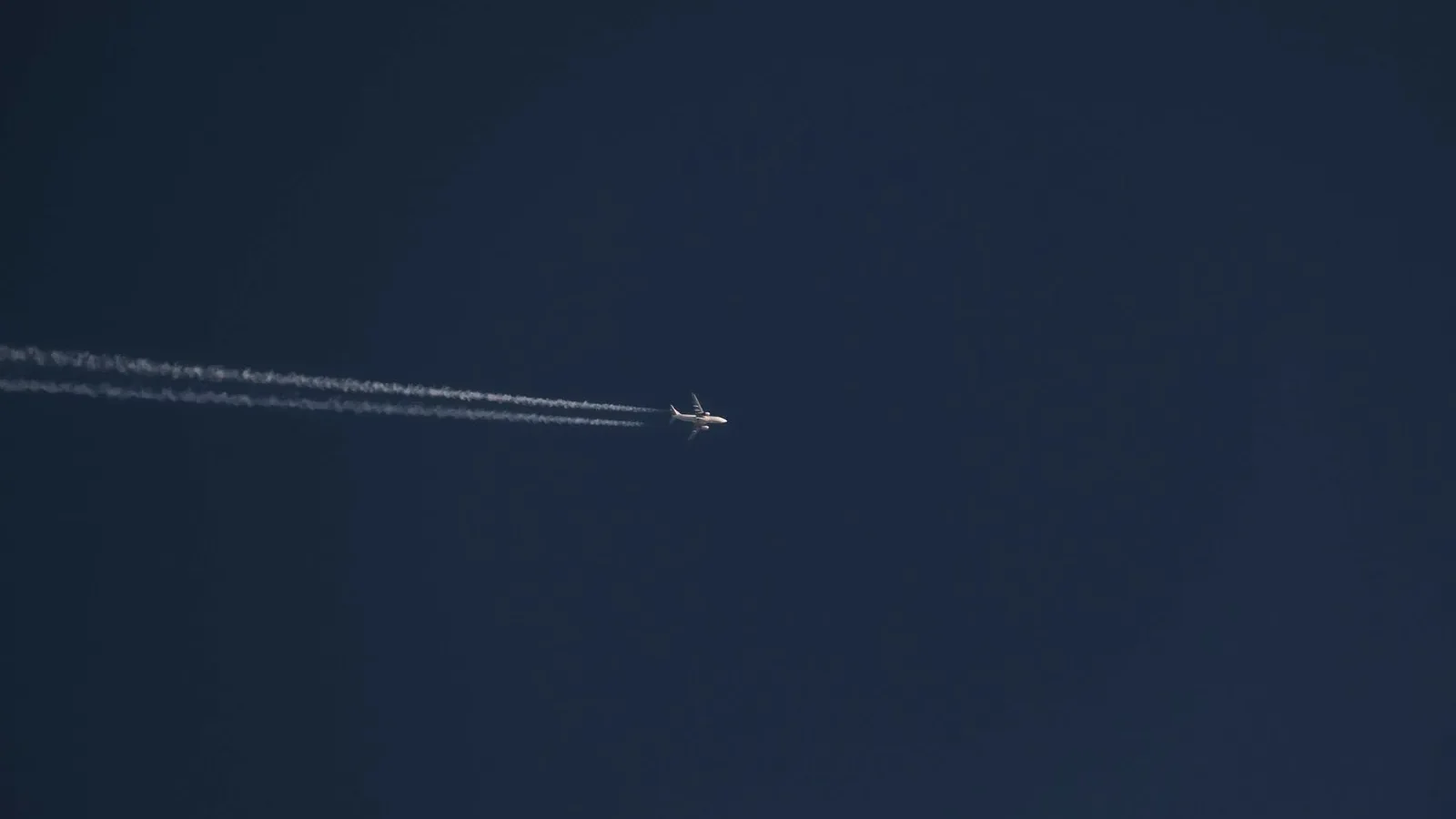 From below of modern distant airplane flying high in air over clear cloudless blue sky with white trace on sunny day.