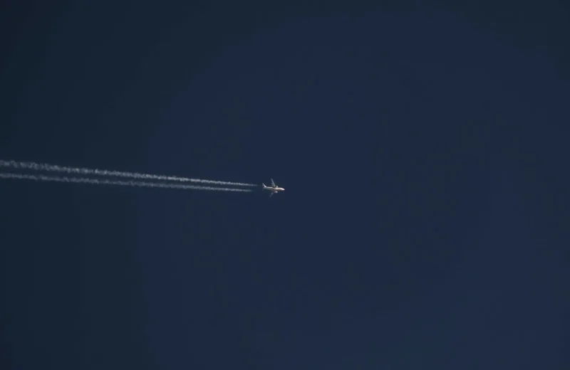 From below of modern distant airplane flying high in air over clear cloudless blue sky with white trace on sunny day.