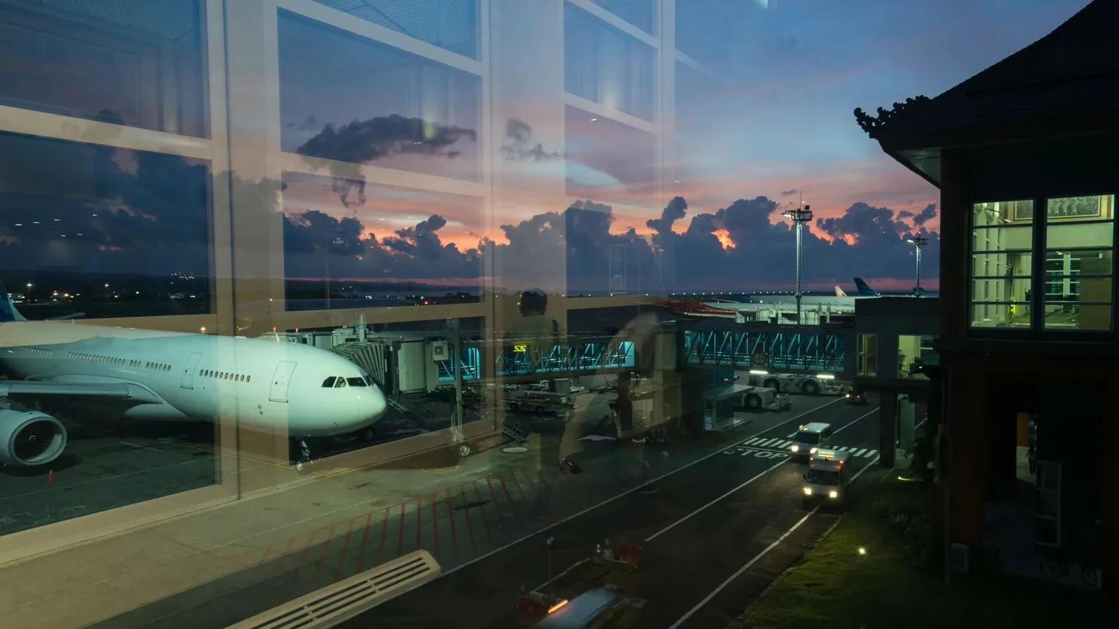 Through glass modern aircraft parked near airbridge in contemporary airport against picturesque dusk sky.
