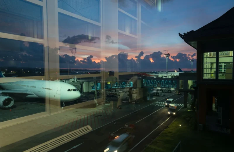 Through glass modern aircraft parked near airbridge in contemporary airport against picturesque dusk sky.