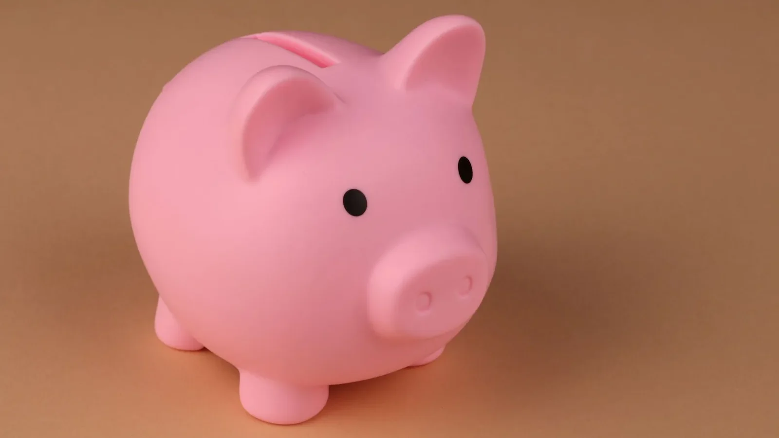 A pink piggy bank symbolizes savings and budgeting on a simple brown backdrop.