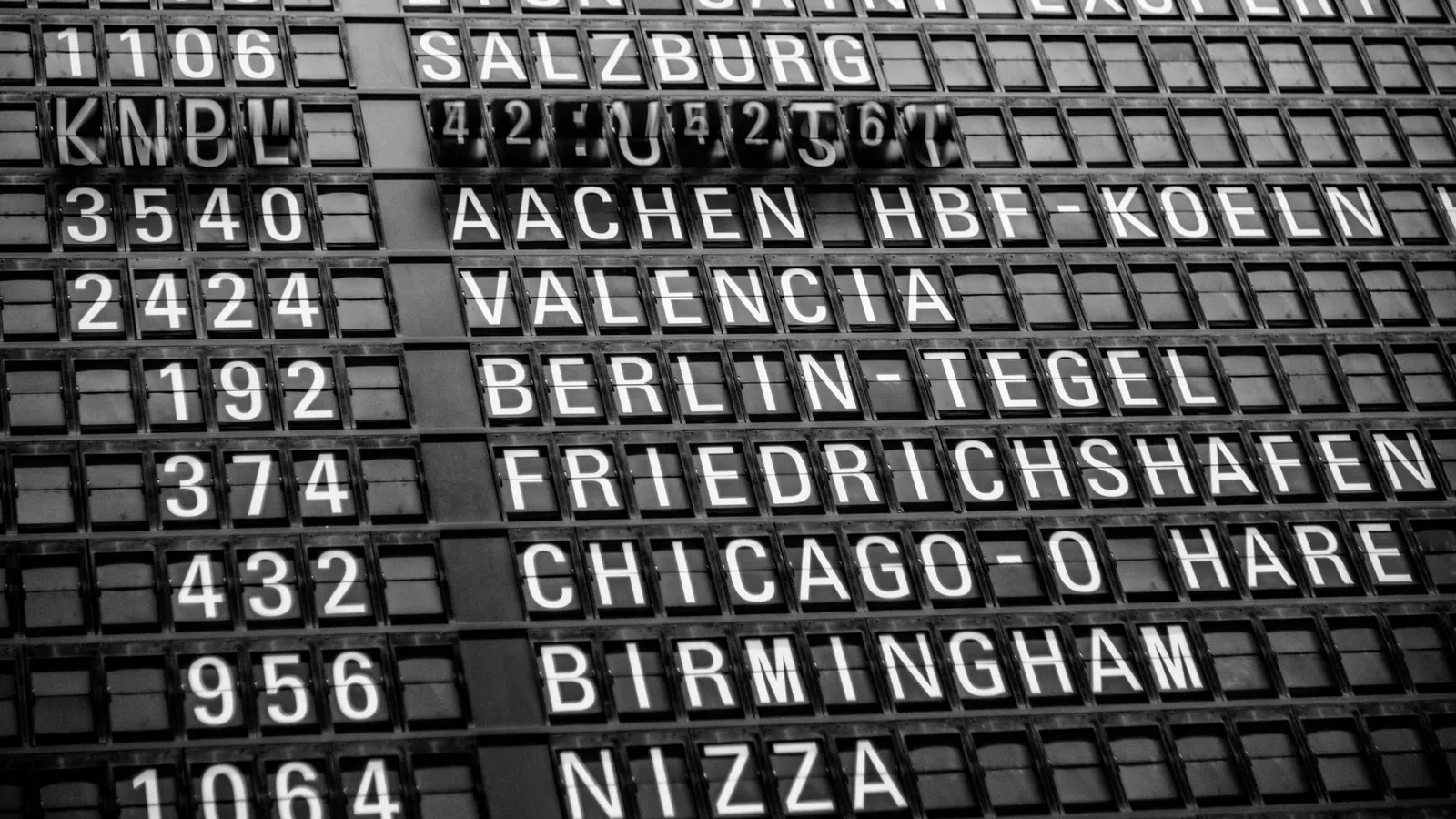 Black and white image of a vintage airport departure board displaying various international destinations.