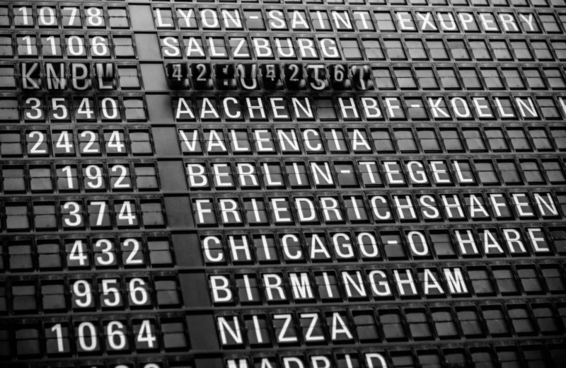 Black and white image of a vintage airport departure board displaying various international destinations.