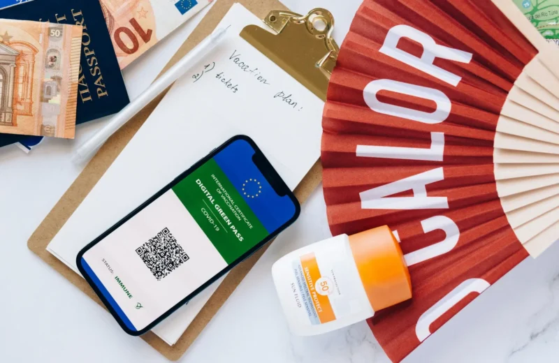 Flat lay of travel essentials featuring a digital green pass, passport, and other travel items on a table.
