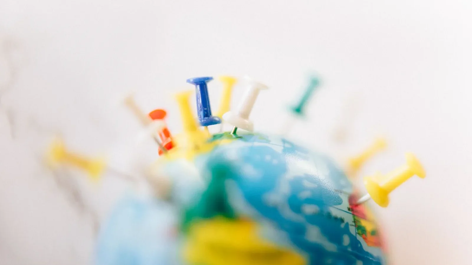 Vibrant close-up of a globe marked with multicolored push pins on a white background.