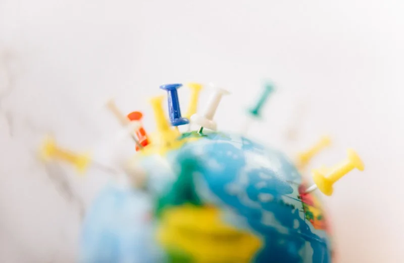 Vibrant close-up of a globe marked with multicolored push pins on a white background.