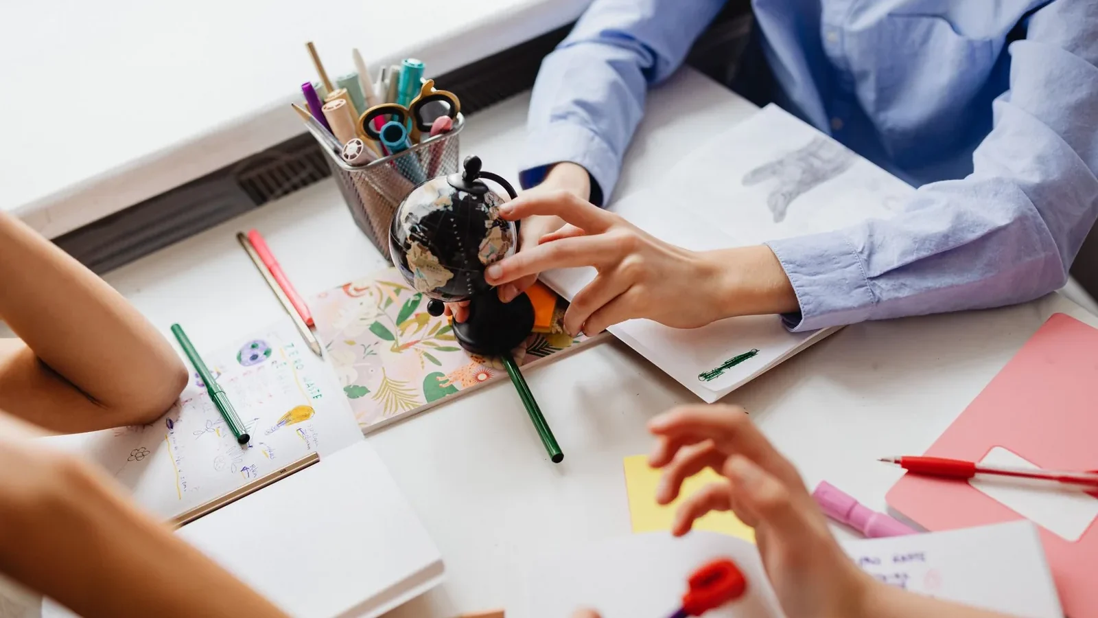 Children engaged in learning with a globe and art supplies on a desk, emphasizing education and creativity.