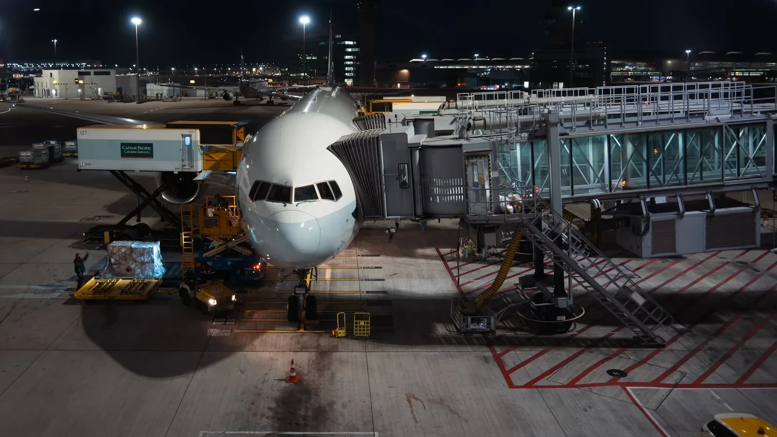 Airplane parked at airport gate during nighttime, unloading cargo and passengers.