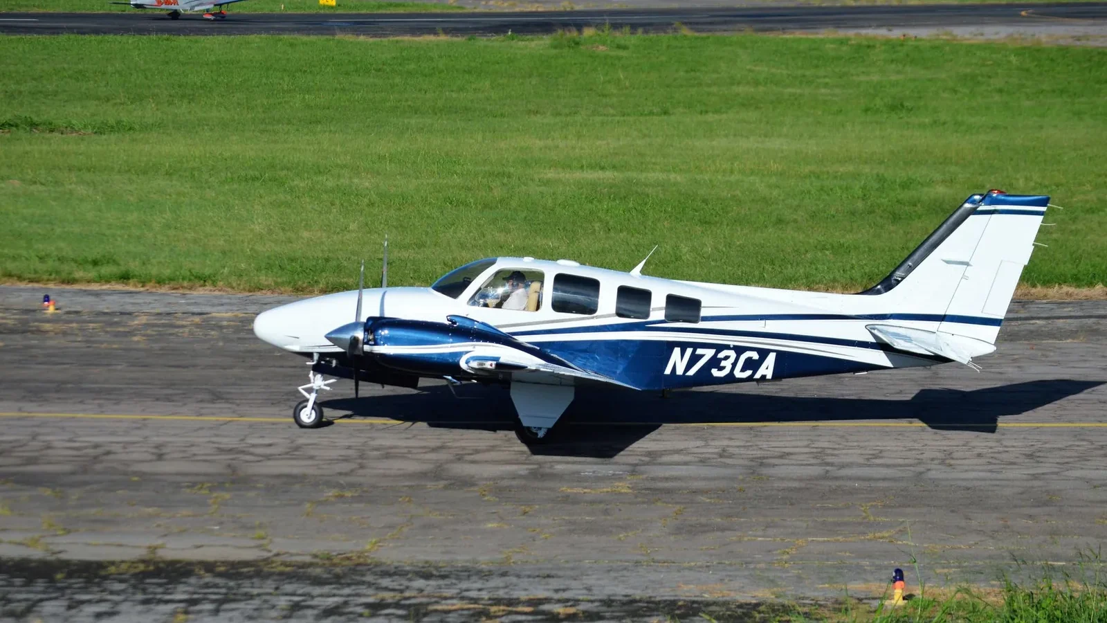 A small aircraft with registration N73CA taxiing on a sunny runway with green grass.