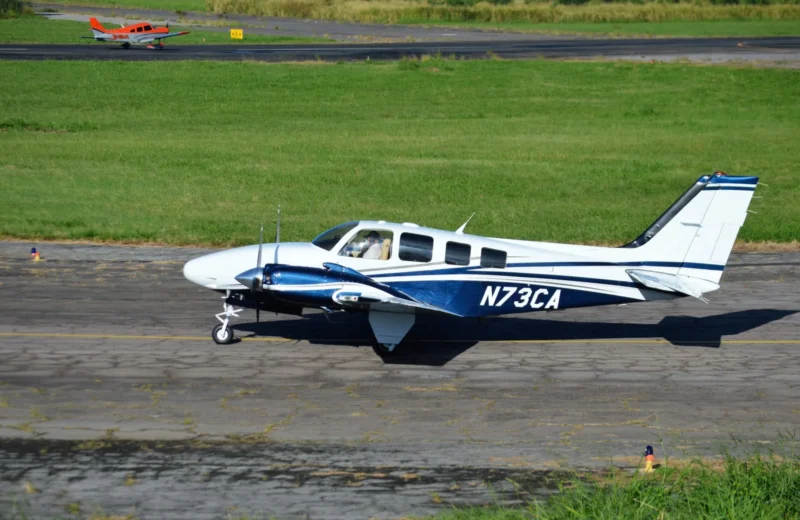 A small aircraft with registration N73CA taxiing on a sunny runway with green grass.