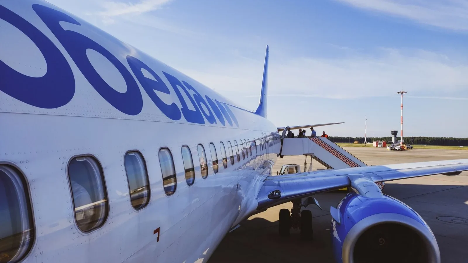 Side view of a commercial airplane with passengers boarding at a sunny airport.