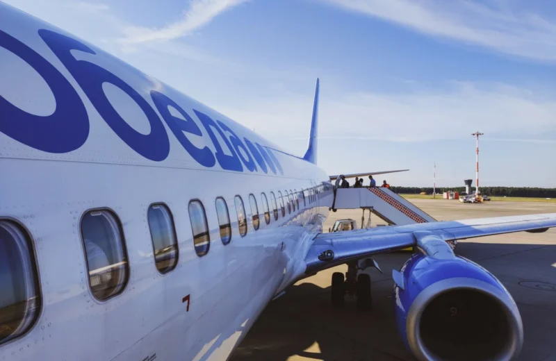 Side view of a commercial airplane with passengers boarding at a sunny airport.