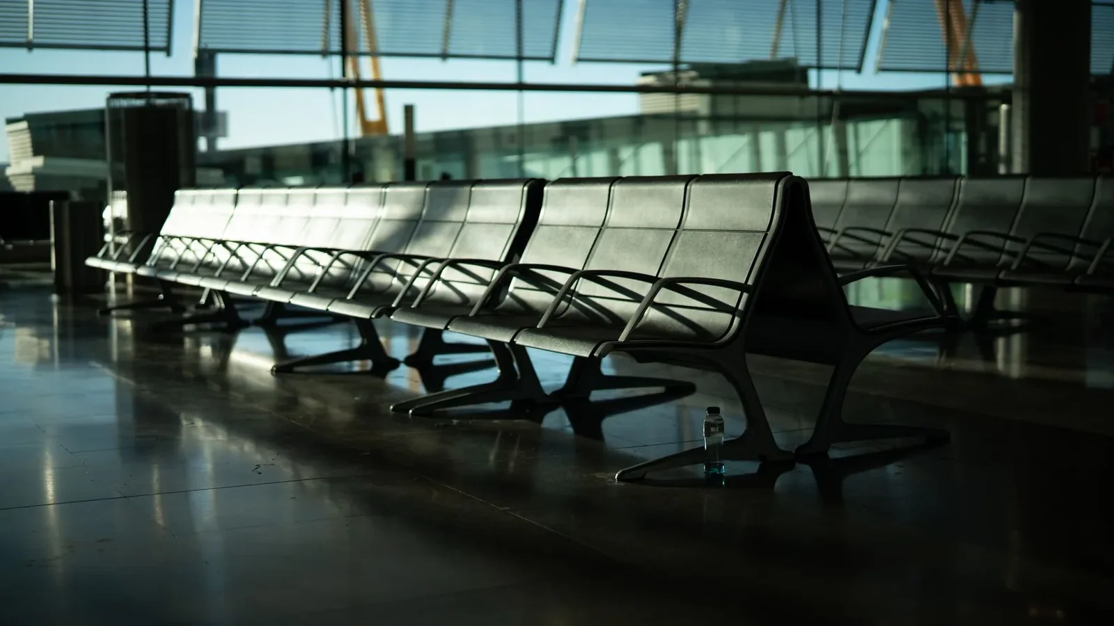 Deserted airport seating area with sunlight streaming through large windows. Calm and quiet atmosphere.