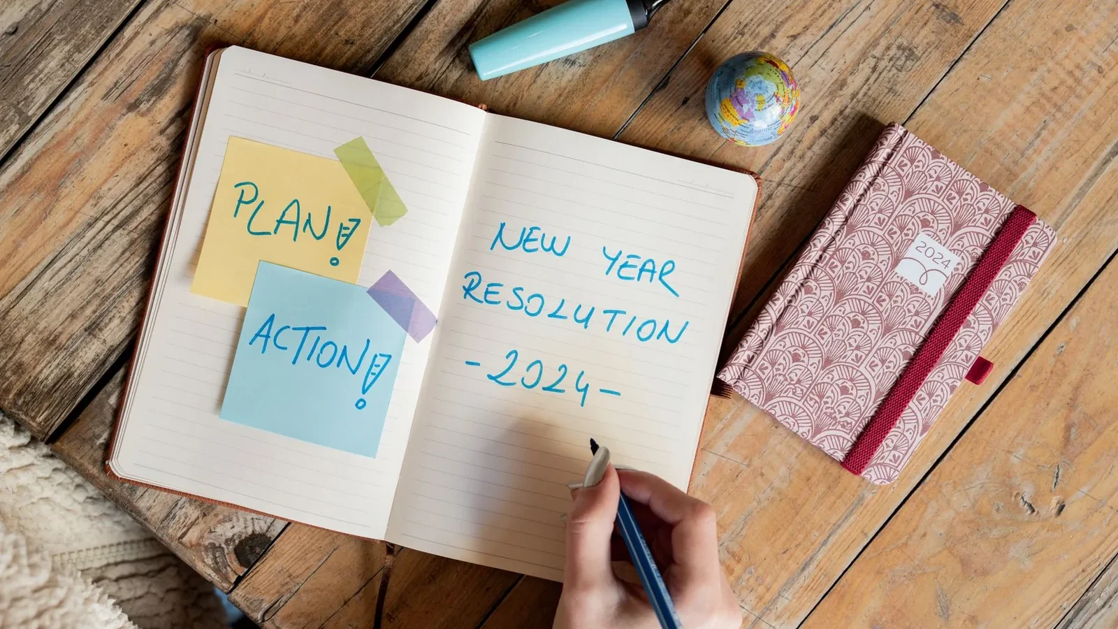 Person writing New Year resolution in a notebook with a pen, symbolizing goal setting for 2024.
