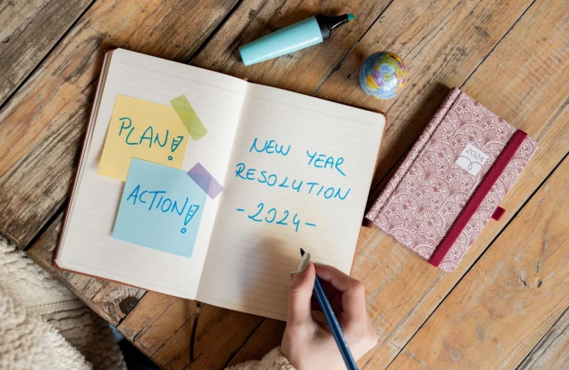 Person writing New Year resolution in a notebook with a pen, symbolizing goal setting for 2024.