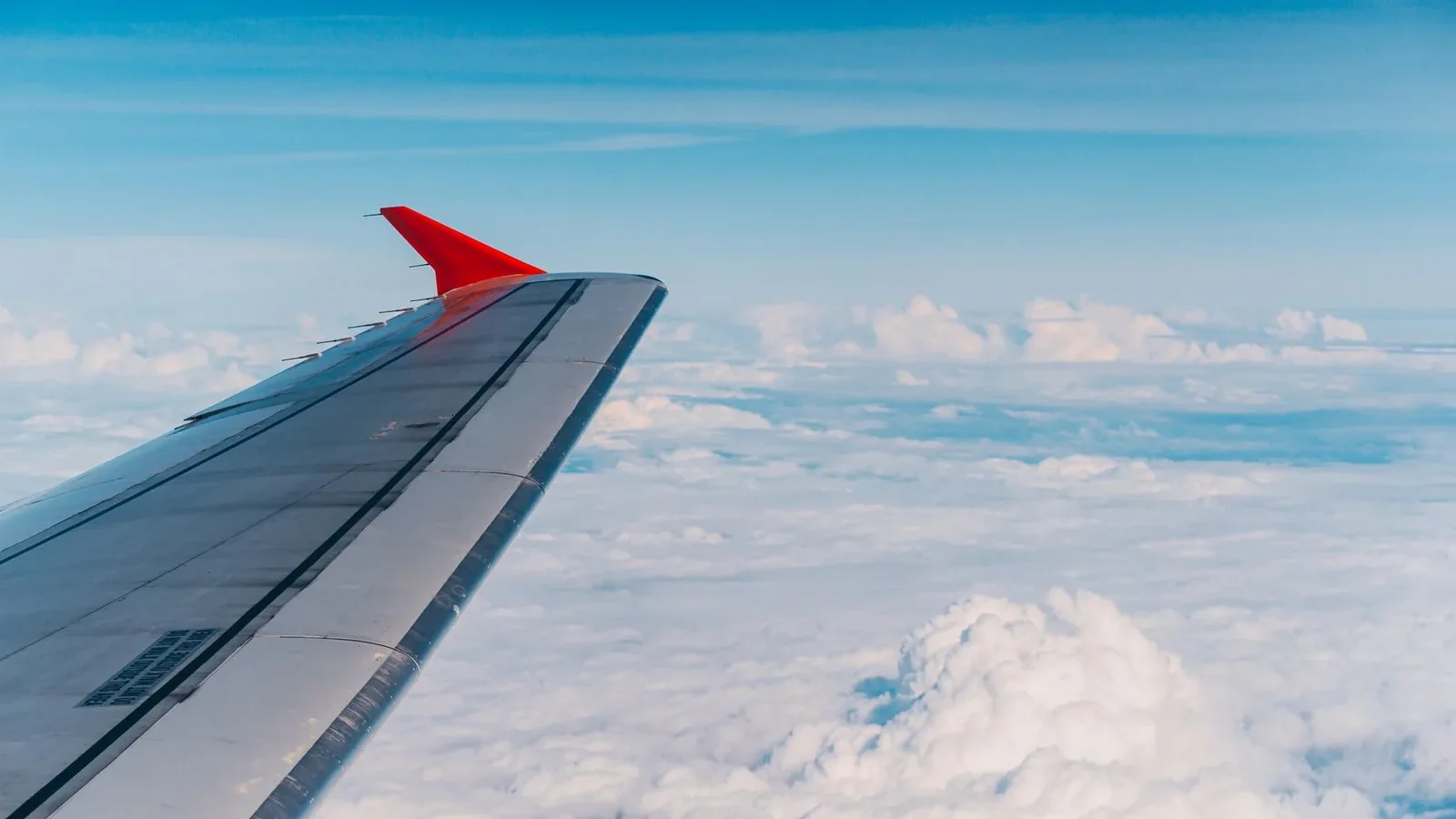 High altitude view of an airplane wing amidst fluffy clouds and blue sky.