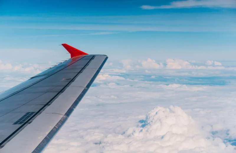 High altitude view of an airplane wing amidst fluffy clouds and blue sky.