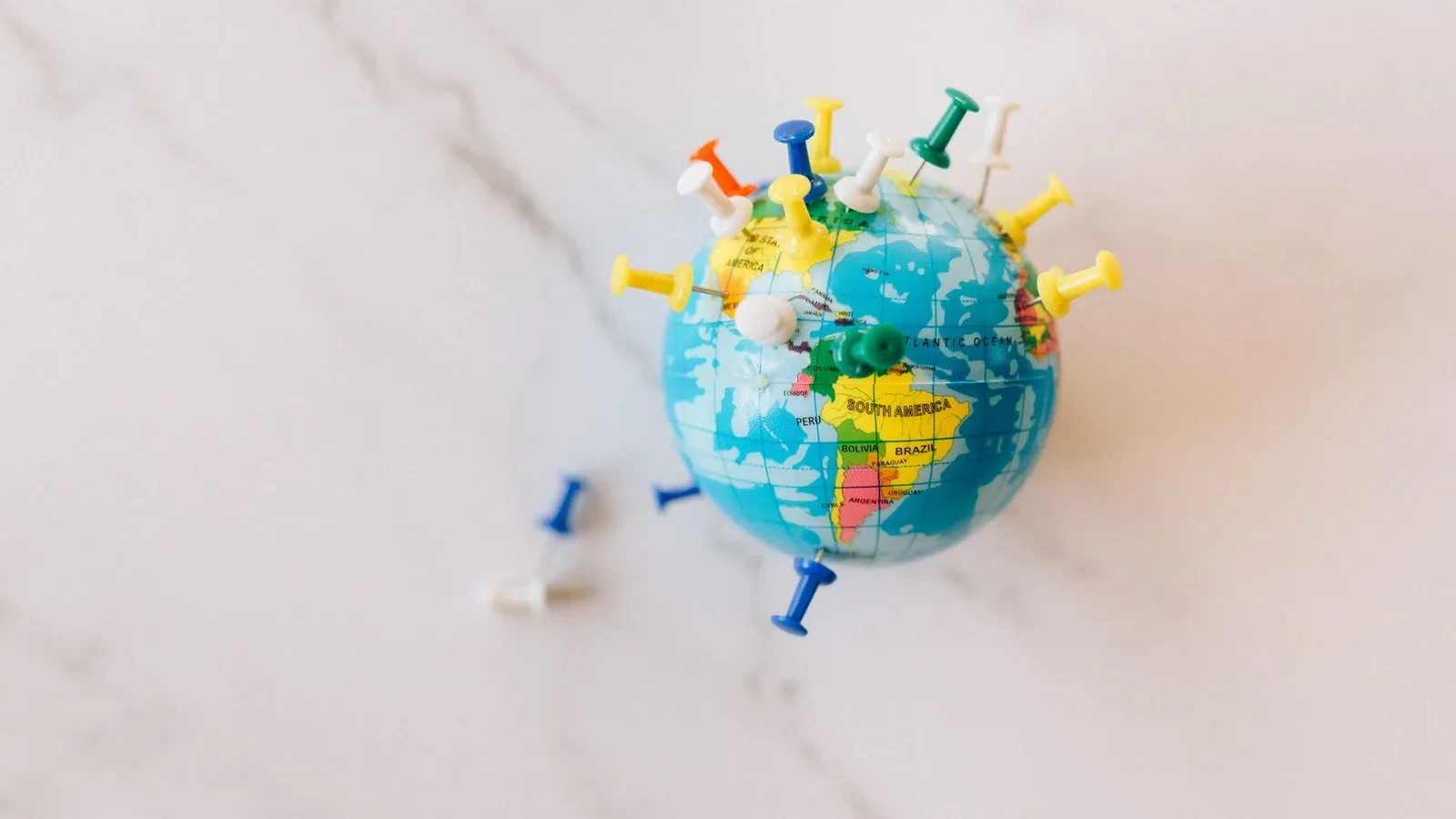 A globe decorated with colorful push pins on a marble surface represents global connections.