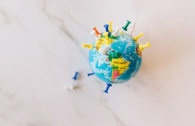 A globe decorated with colorful push pins on a marble surface represents global connections.