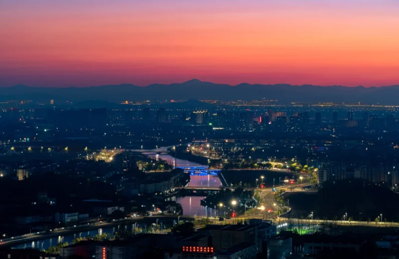 A vibrant cityscape at twilight showcasing a glowing skyline and a colorful sunset horizon.