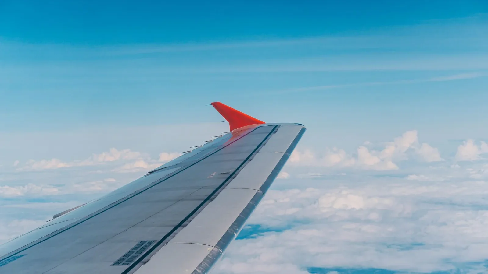 Aerial view from plane showcasing airplane wing above fluffy clouds and blue sky.