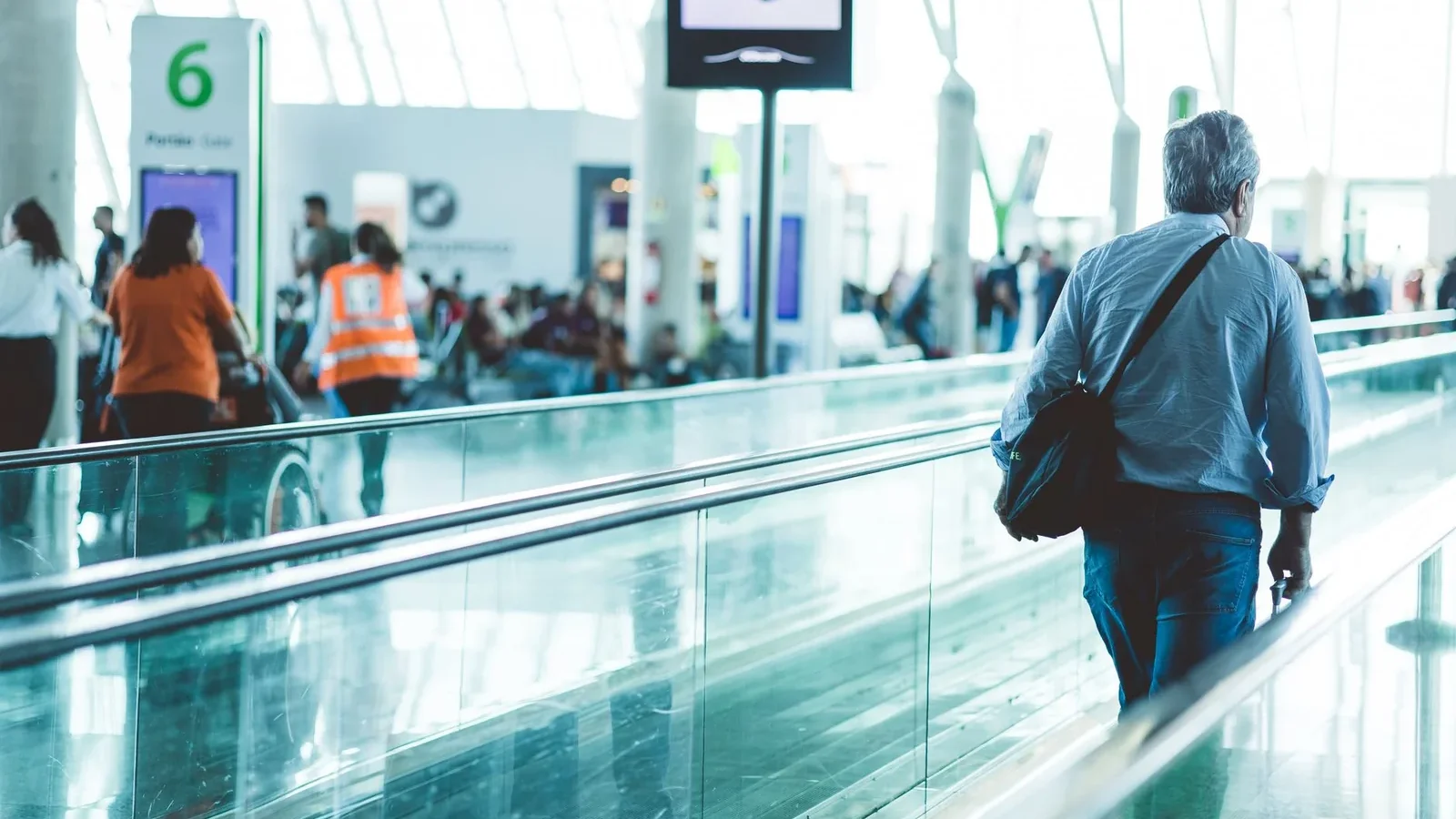 A bustling airport scene with travelers on a moving walkway in a modern terminal.