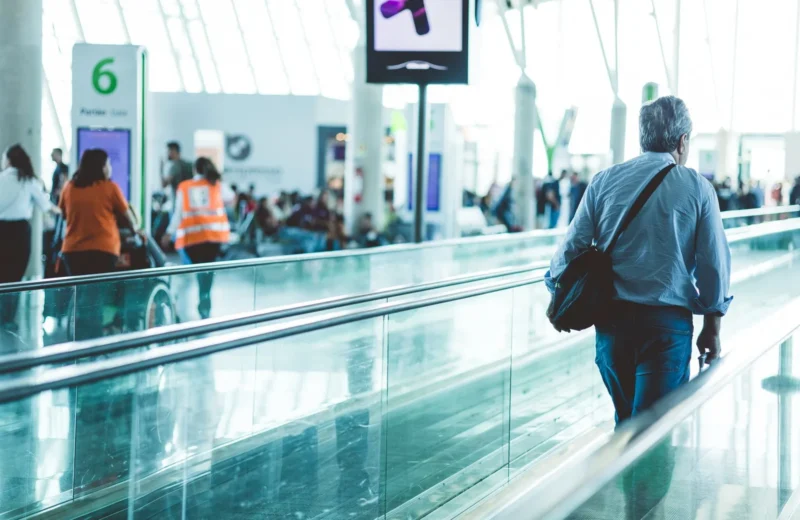 A bustling airport scene with travelers on a moving walkway in a modern terminal.