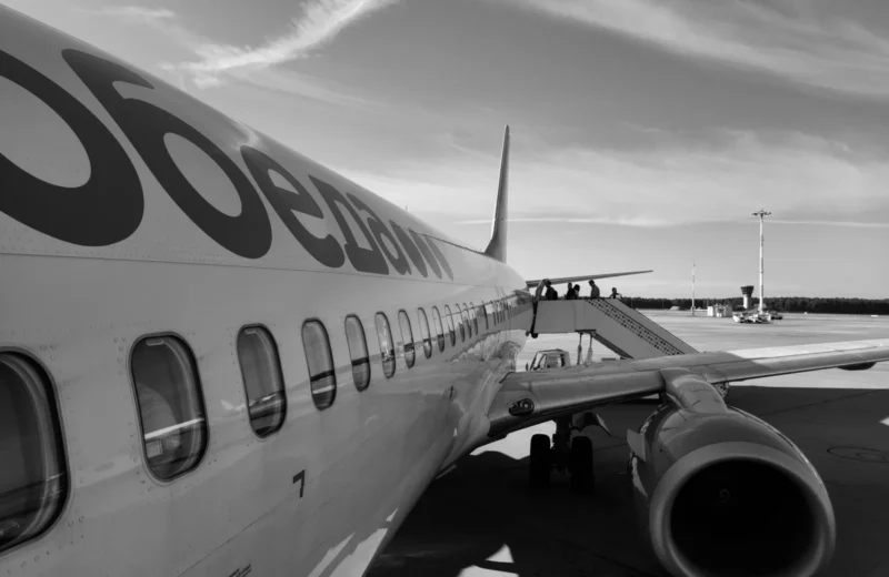 Monochrome image of an airplane on the tarmac with passengers boarding via stairs.
