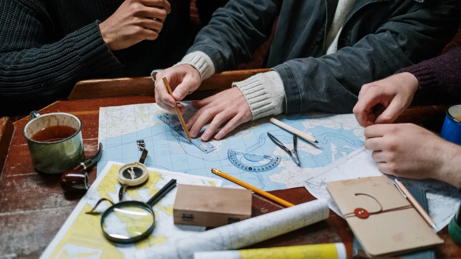 Adults planning a nautical journey using maps, compass, and tools indoors.