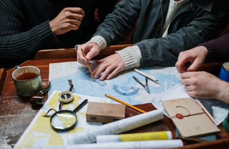Adults planning a nautical journey using maps, compass, and tools indoors.