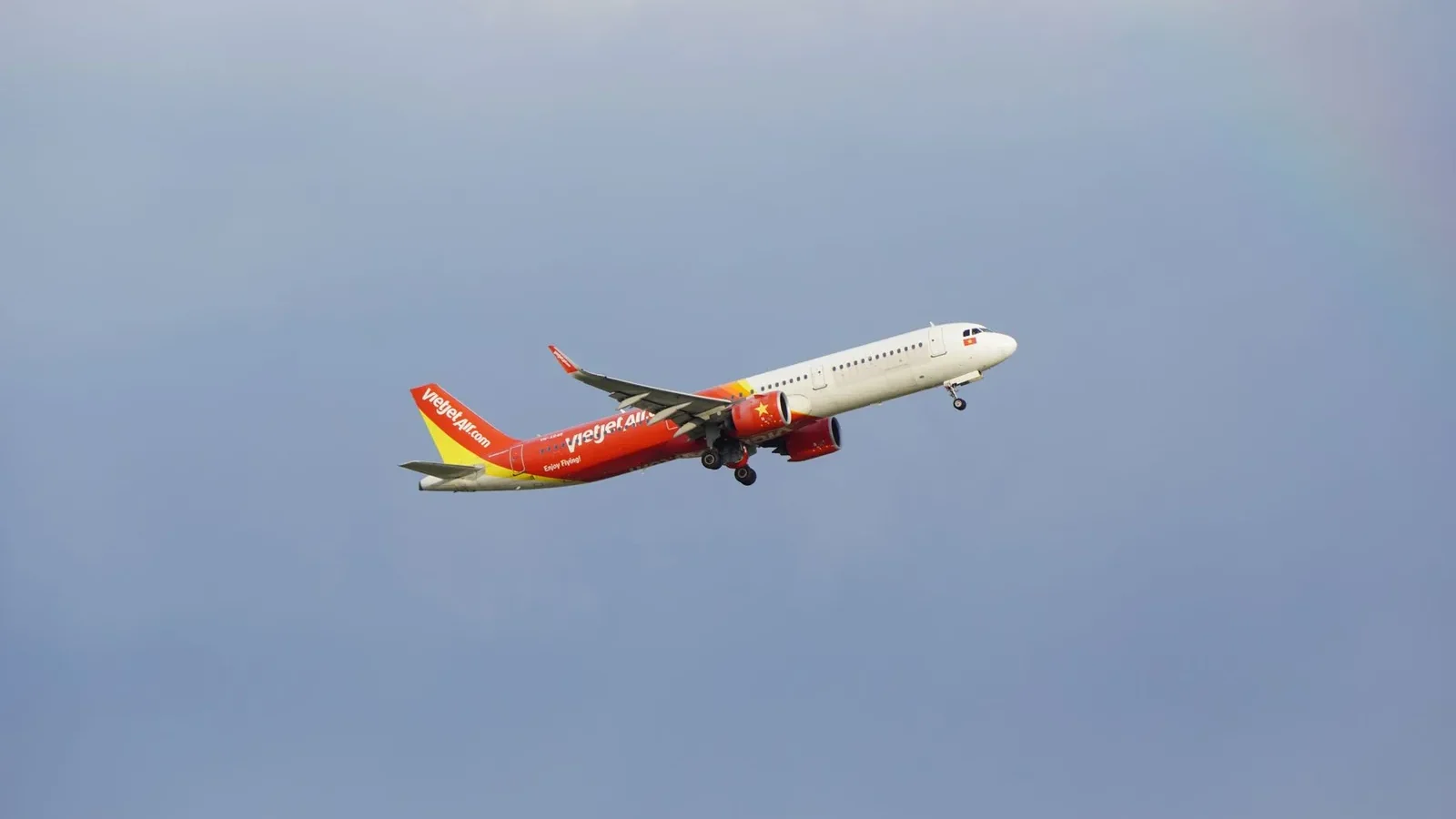 An airplane from the airline VietJet in mid-flight against a clear blue sky.