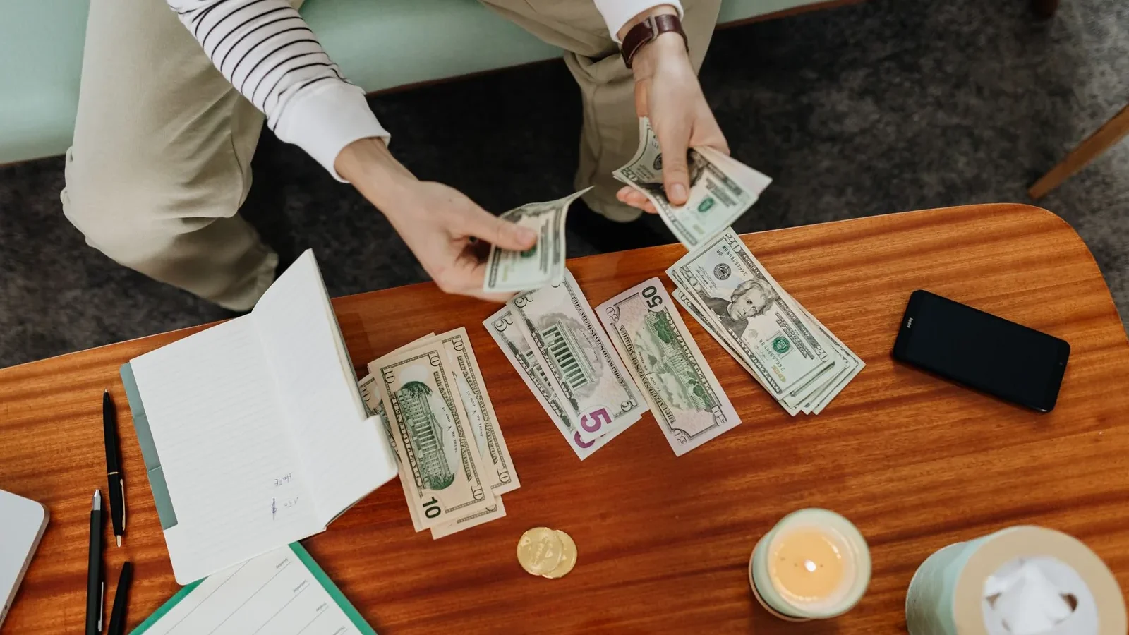 A person sitting and counting various US dollar bills at a table indoors.
