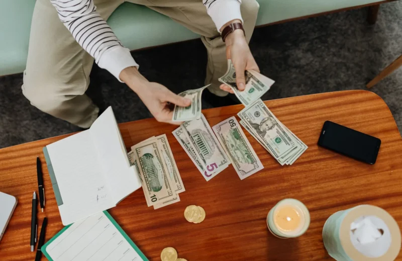 A person sitting and counting various US dollar bills at a table indoors.