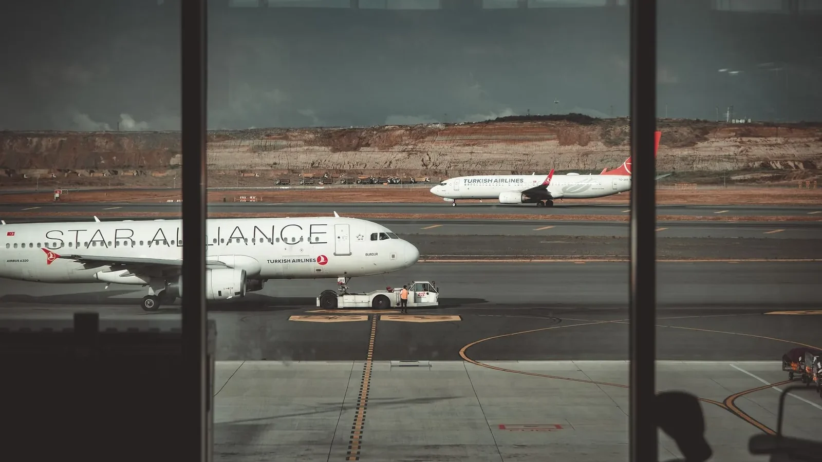 A view through airport windows showing airliners on the runway, creating a travel ambiance.