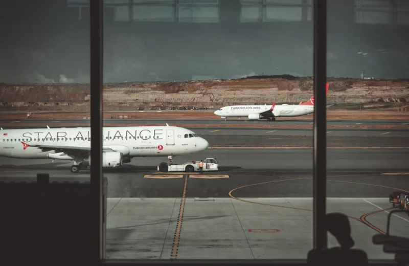 A view through airport windows showing airliners on the runway, creating a travel ambiance.