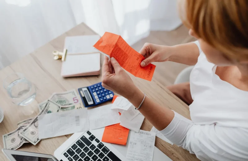 Woman using calculator and receipts at home office desk for finance management.