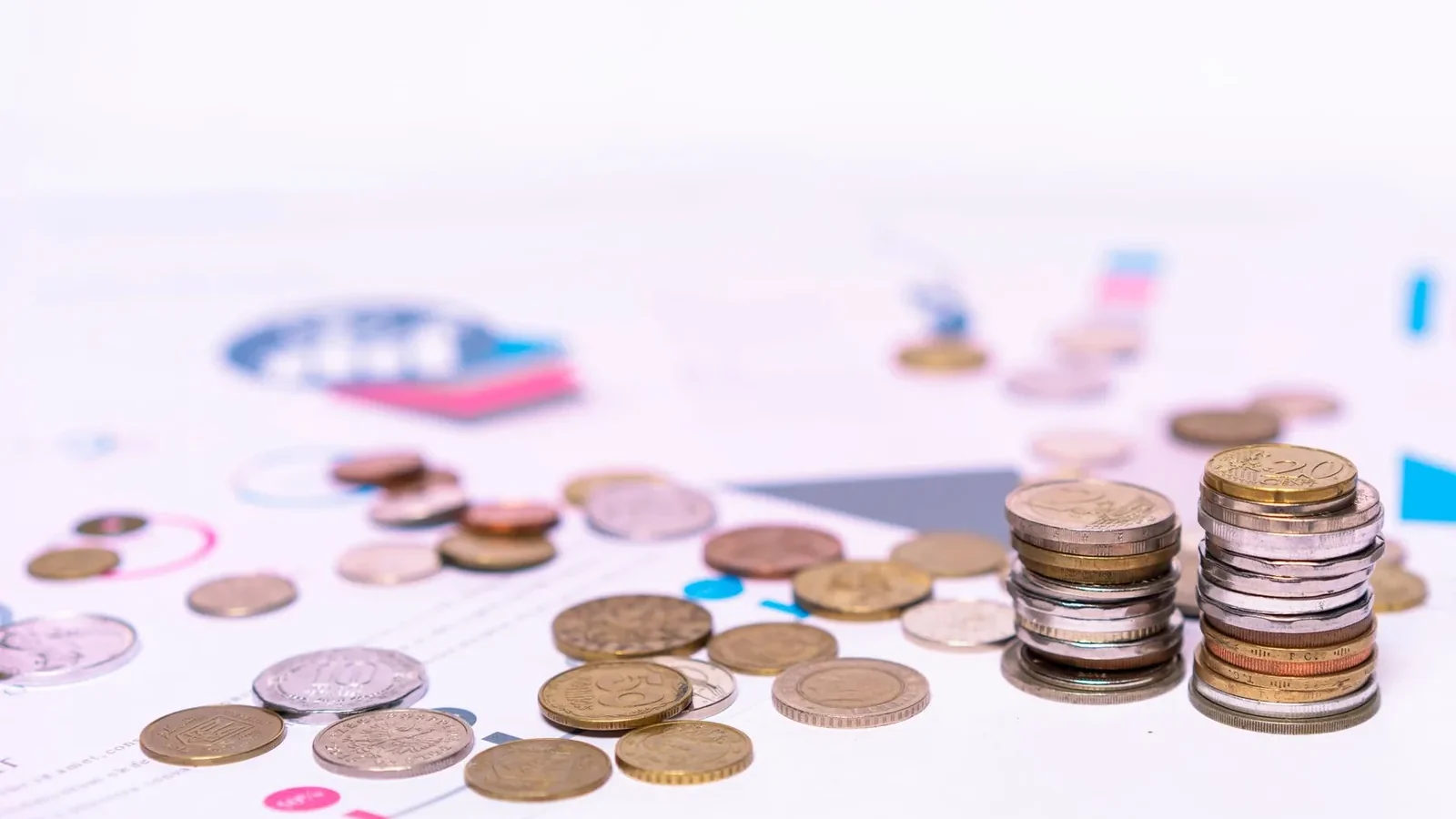 Stack of assorted coins with financial documents on a white background, highlighting the concept of savings.
