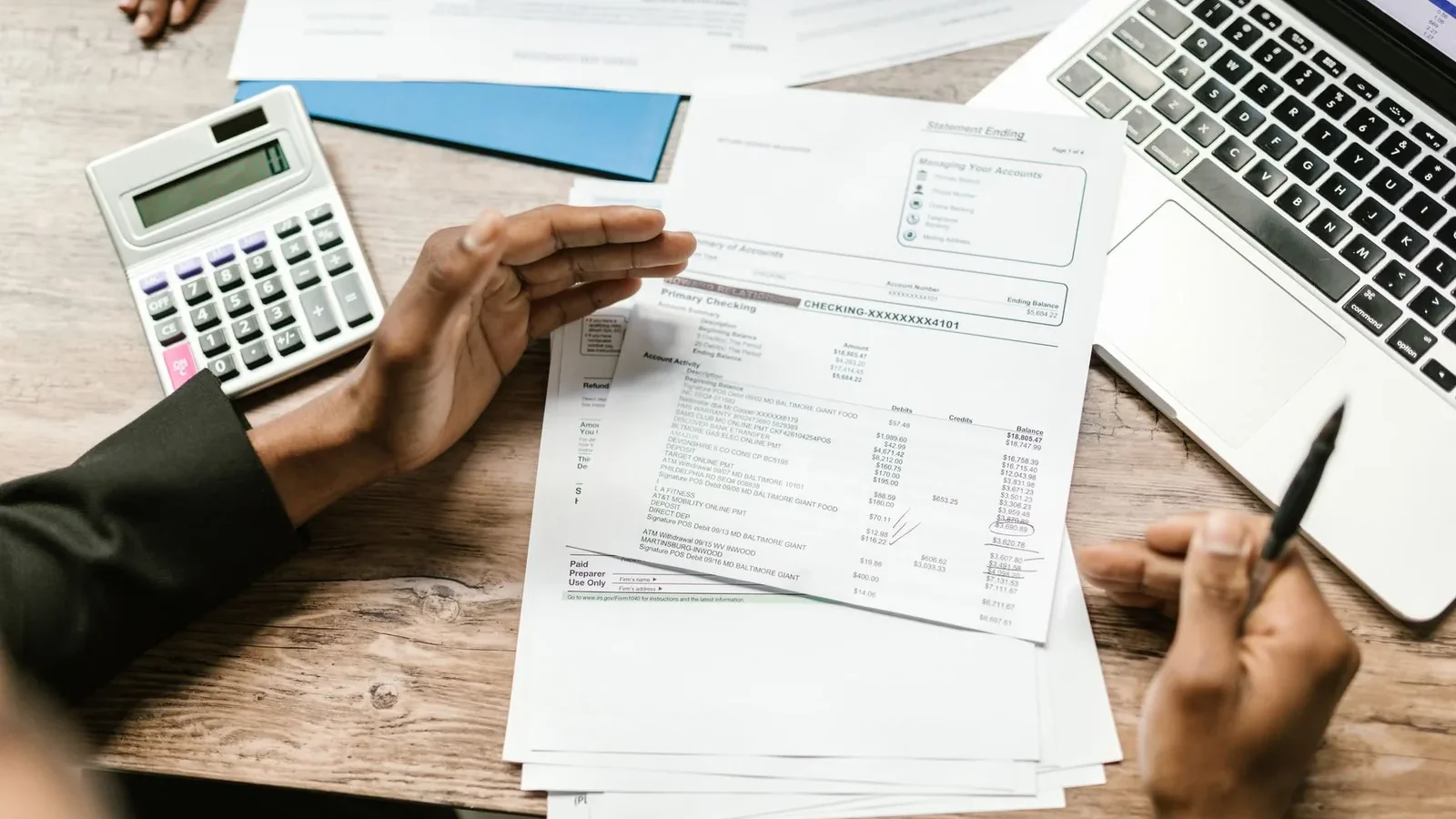 Hands holding financial documents with calculator and laptop on office desk, business analysis scene.