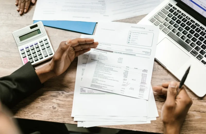 Hands holding financial documents with calculator and laptop on office desk, business analysis scene.