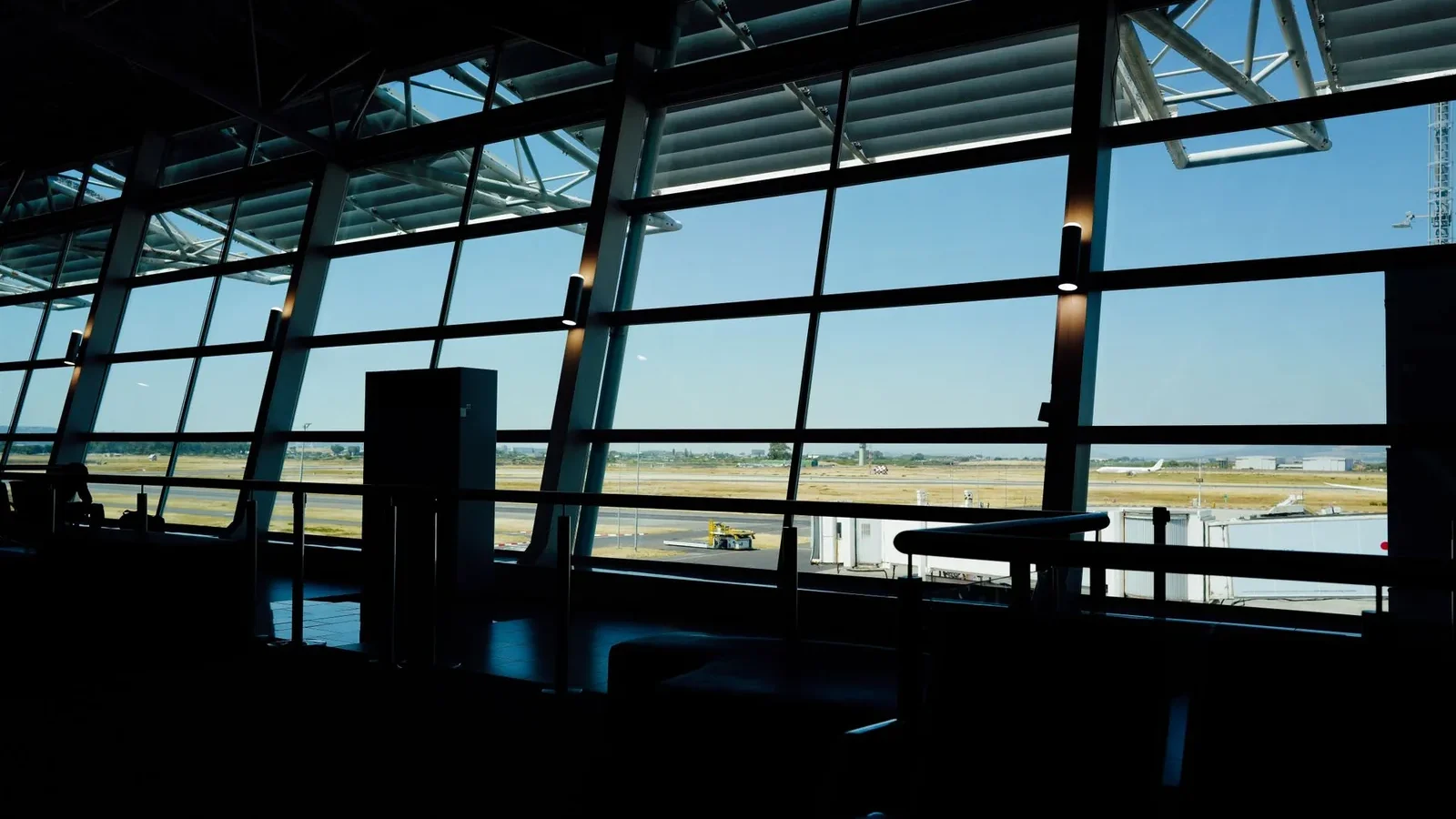 View from inside an airport terminal overlooking the runway under a bright blue sky.