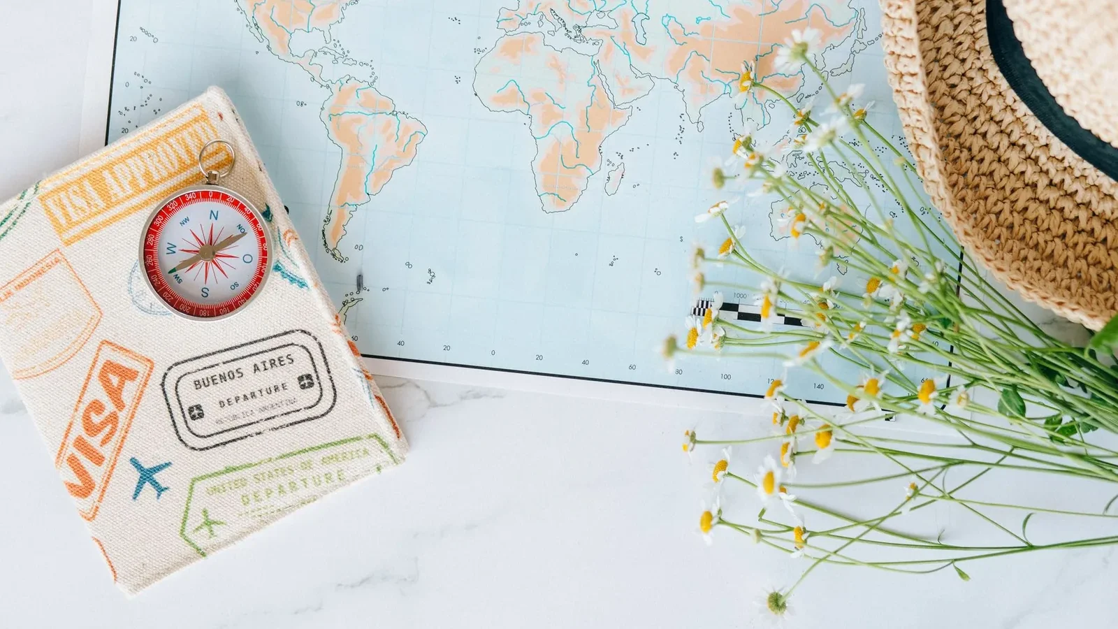 Flat lay of world map, compass, passport, and chamomile flowers, perfect for travel enthusiasts.