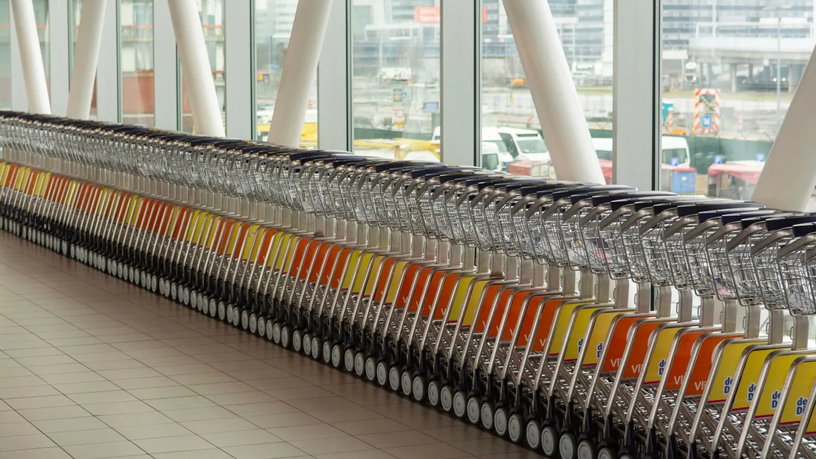 A row of luggage carts neatly lined up inside Schiphol Airport in Amsterdam.