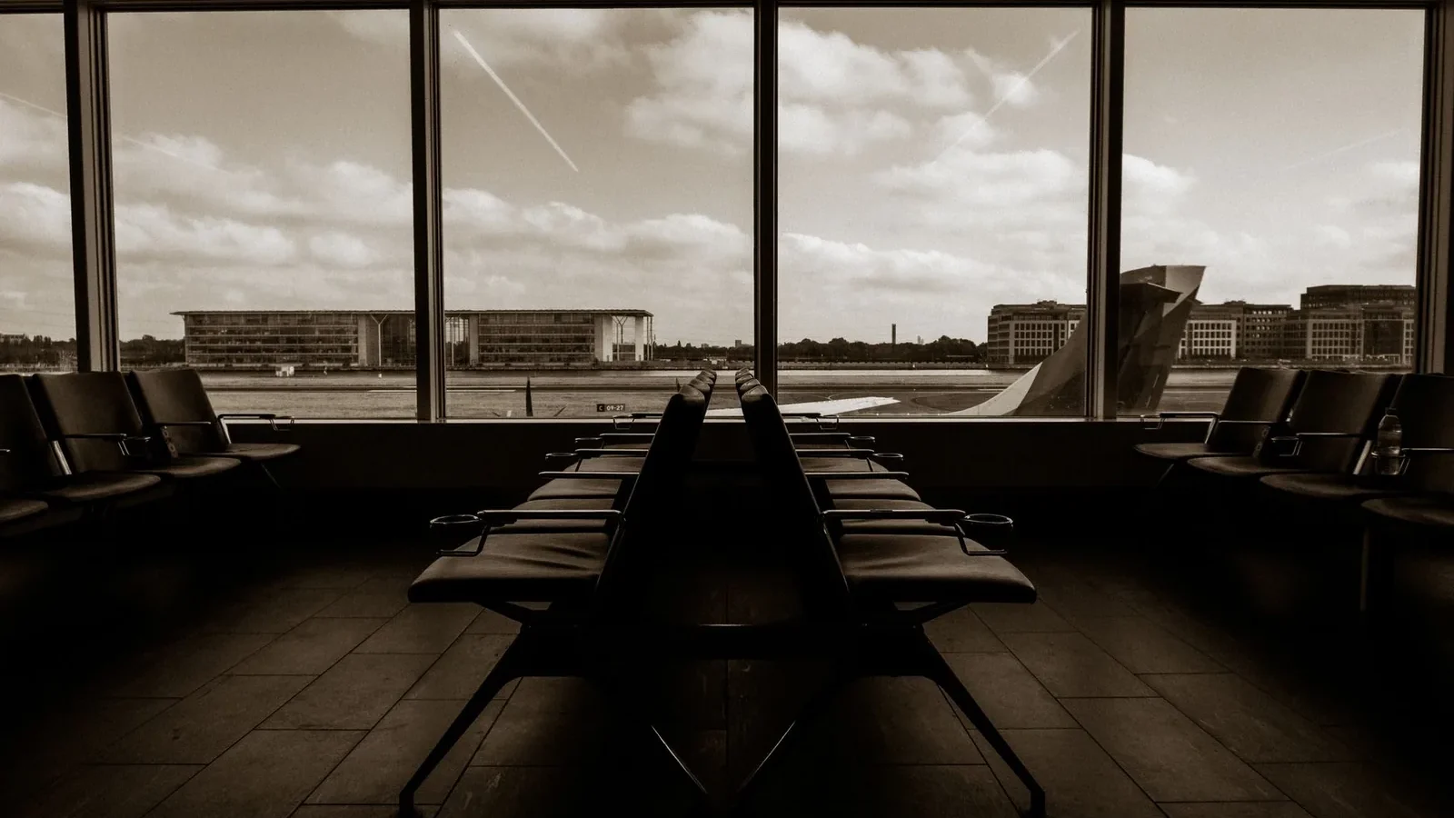 Quiet airport terminal in sepia tone overlooking runway and airplane wing.