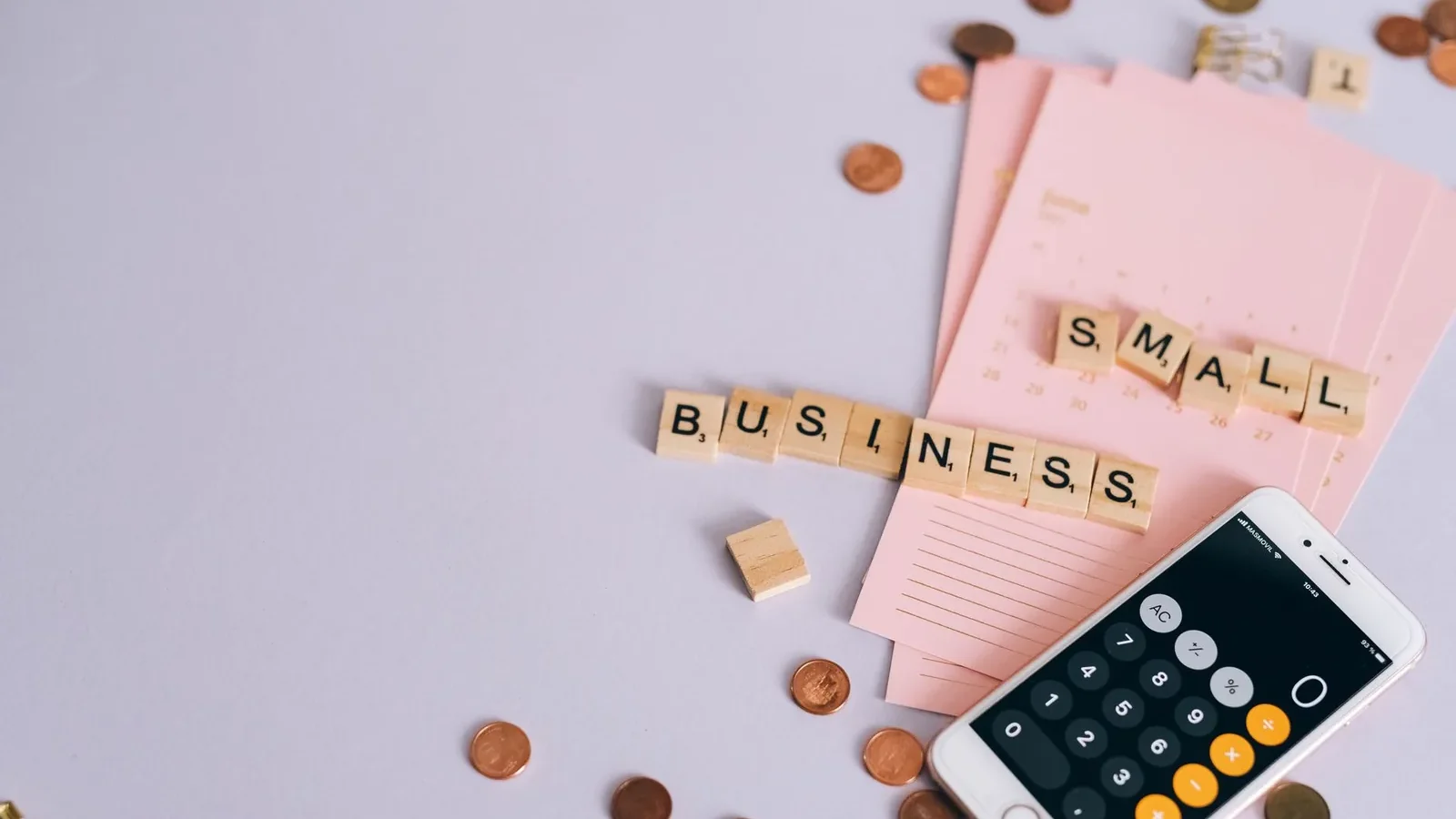 Flat lay of a small business planning scene with coins, smartphone calculator, and letter tiles.