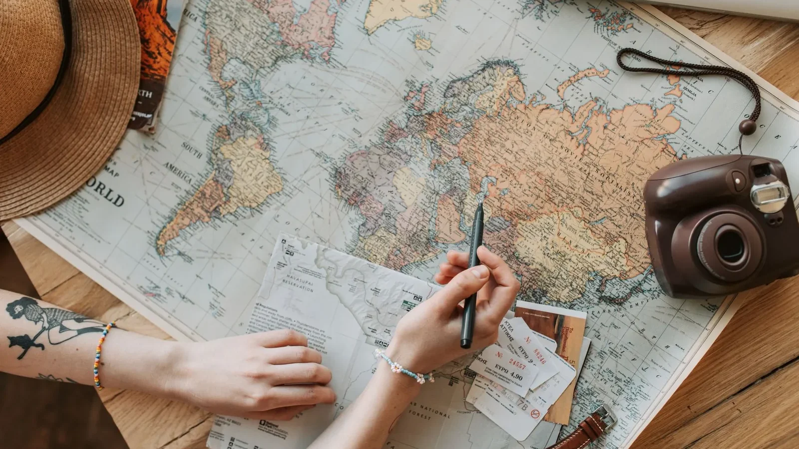 Top view of a woman's hands planning a trip with a map, camera, and travel items.