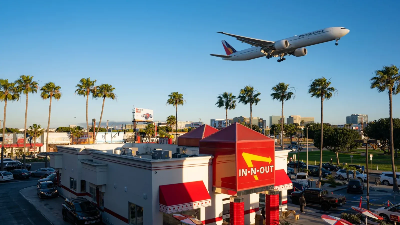A plane flying over In-N-Out Burger with palm trees in Los Angeles, California.